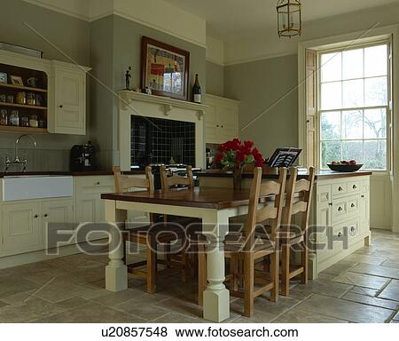 Stock Photo - Wooden chairs at fitted table on island unit in grey kitchen with cream fitted units. Fotosearch