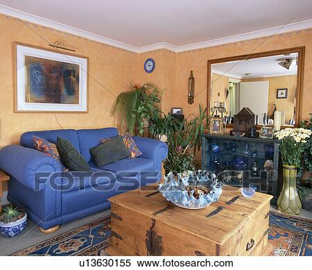 Stock Photography - Wooden chest in front of blue sofa in ochre living room. Fotosearch
