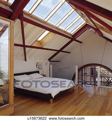 Stock Image - Wooden flooring and glass apex ceiling in modern loft conversion bedroom. Fotosearch