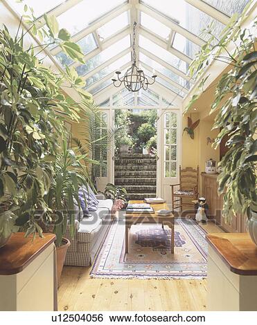 Stock Photograph - Wooden flooring and lush houseplants in traditional glass conservatory with doors open to garden. Fotosearch
