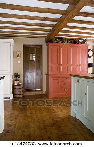 Stock Image - Wooden flooring in beamed country kitchen with large terracotta cupboard beside back door. Fotosearch