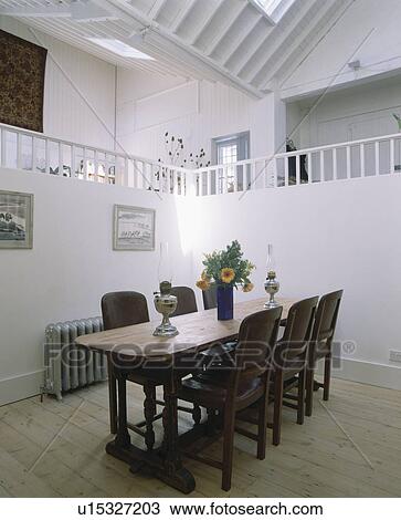 Stock Image - Wooden furniture and floor in white dining room in small modern loft conversion. Fotosearch