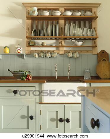 Picture - Wooden plate rack above white Belfast sink in kitchen with pale green fitted units. Fotosearch