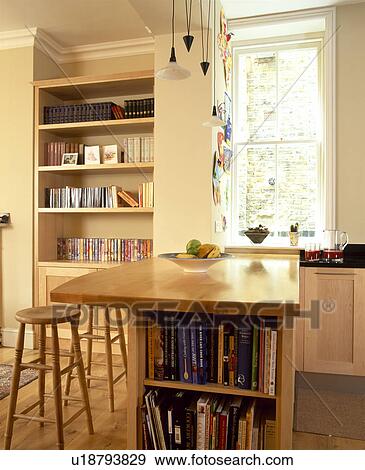 Stock Photo - Wooden stools at island breakfast bar with integral bookshelves in traditional kitchen. Fotosearch