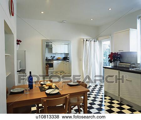 Stock Photo - Wooden table and chairs in modern kitchen with black+white chequerboard flooring. Fotosearch