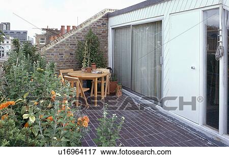 Stock Photo - Wooden table and chairs on paved roof garden of small loft conversion with patio doors. Fotosearch