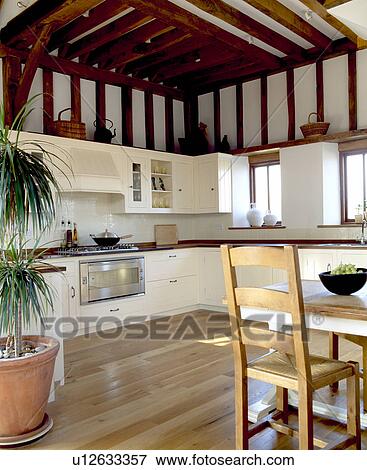 Stock Photo - Wooden table and flooring in beamed country kitchen with fitted cream cupboards. Fotosearch