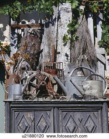 
 Decorative outdoor garden cupboard with implelements including galvanised watering cans overhung with hazel on a paling fence. View Large Photo Image Stock Image - 
 Decorative outdoor garden cupboard with implelements including galvanised watering cans overhung with hazel on a paling fence.. Fotosearch