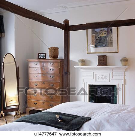 Stock Photo - Antique Georgian chest-of-drawers beside fireplace in small traditional bedroom. Fotosearch