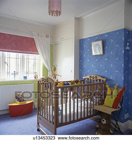 Stock Image - Baby's wooden cot in nursery bedroom with pink blind and wall with blue wallpaper. Fotosearch