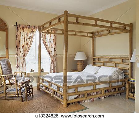 Stock Photograph - Bamboo four-poster bed and cream chaiselongue in Spanish bedroom. Fotosearch