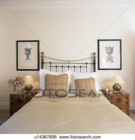 Stock Photograph - Beige cushions and bedcover on brass bed in townhouse bedroom. Fotosearch