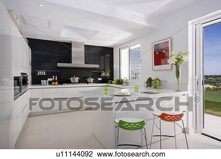 Stock Image - Black and white kitchen with touches of red and green overlooking countryside.. Fotosearch