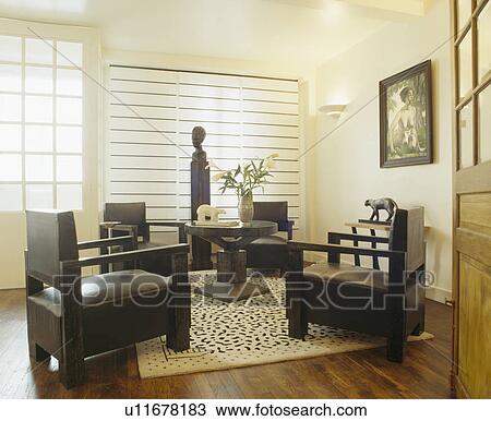 Stock Image - Black forties style armchairs and abstract patterned cream rug in modern white livingroom with sculpture head on plinth. Fotosearch
