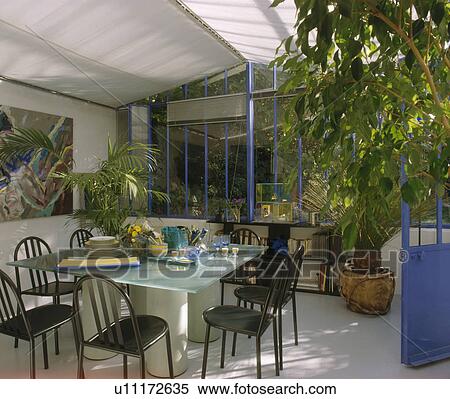 Stock Photography - Black metal chairs and glass-topped table in modern conservatory dining room. Fotosearch