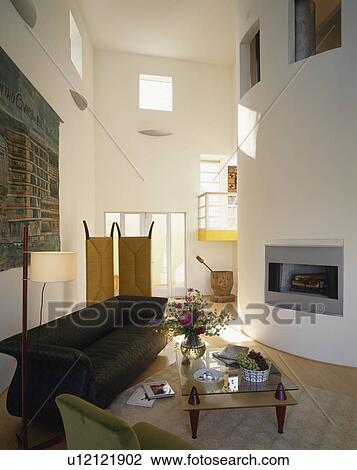 Black sofa in large double-height modern living room with fireplace in curved wall View Large Photo Image Stock Image - Black sofa in large double-height modern living room with fireplace in curved wall. Fotosearch