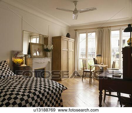 Stock Photo - Black+white checked bedlinen on bed in apartment bedroom with ceiling fan and parquet floor. Fotosearch