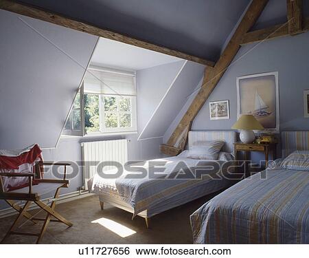 Stock Photograph - Blue striped quilts and pillows on twin beds in pastel blue attic bedroom. Fotosearch
