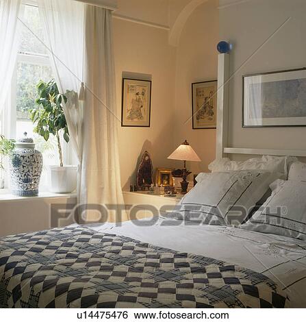 Stock Photograph - Blue+white patchwork quilt on bed in white bedroom. Fotosearch