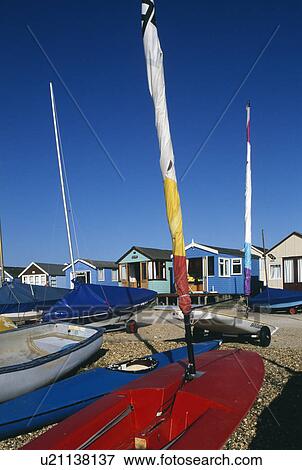 Stock Photo - Boats and brighly coloured windsails with row of beach huts in background at Mudeford in Hampshire. Fotosearch