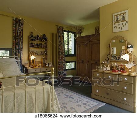 Brass bed and pine chest-of-drawers in traditional country bedroom with lighted lamps View Large Photo Image Picture - Brass bed and pine chest-of-drawers in traditional country bedroom with lighted lamps. Fotosearch