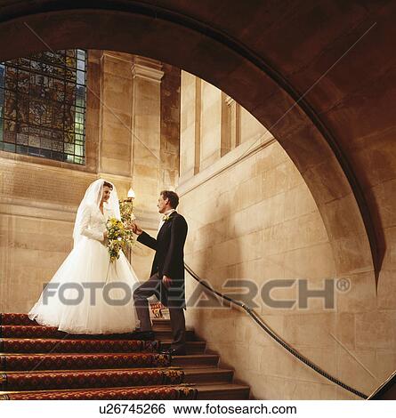 Stock Photograph - Bride and groom on staircase in large hall with stone walls. Fotosearch