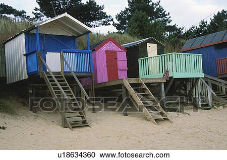 Stock Image - Brightly painted beach huts with wooden ladders on a sandy beach in Norfolk. Fotosearch