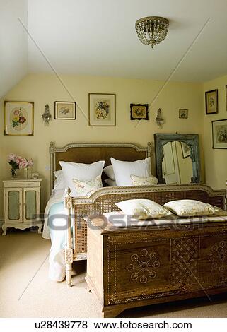 Carved antique chest and French bed in cream country bedroom with floral pictures on the walls View Large Photo Image Stock Photo - Carved antique chest and French bed in cream country bedroom with floral pictures on the walls. Fotosearch