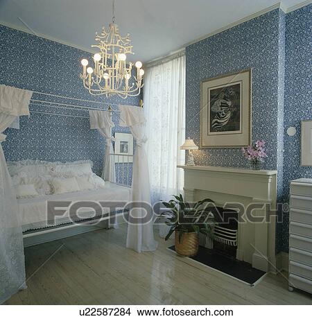 Picture - Chandelier in bedroom with blue floral wallpaper and white bed and fireplace. Fotosearch