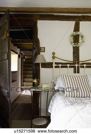 Circular bedside table beside brass bed with striped cushion in beamed country bedroom View Large Photo Image Stock Photo - Circular bedside table beside brass bed with striped cushion in beamed country bedroom. Fotosearch