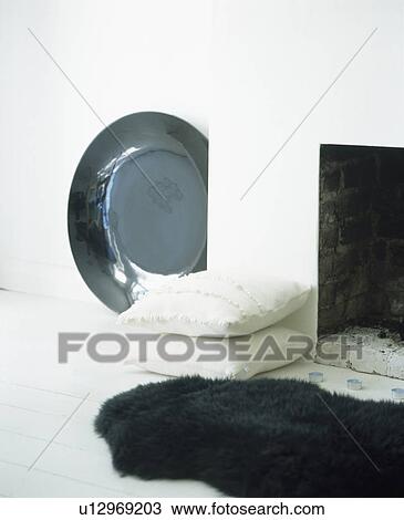 Stock Image - Close-up of black sheepskin rug and white cushions. Fotosearch