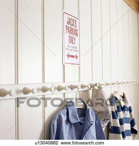 Stock Image - Close-up of clothes on white peg-rail on white panelled wall. Fotosearch