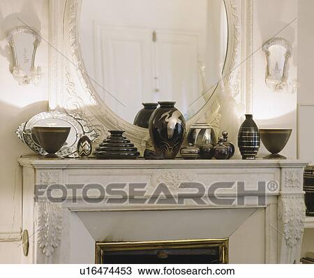 Stock Image - Close-up of collection of black+gilt vases on ornate marble mantelpiece. Fotosearch