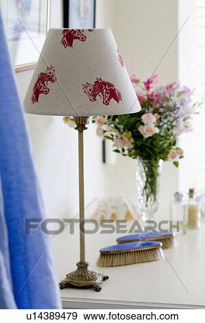 Stock Photo - Close-up of lamp with cream linen lampshade with red horse motif on dressing table ith blue enamelled brushes. Fotosearch