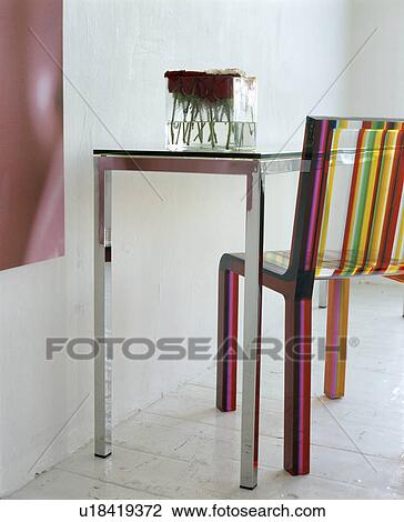Stock Image - Close-up of metal table and multi-coloured striped perspex chair. Fotosearch