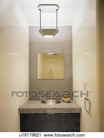 Stock Image - Close-up of mirror in concrete splashback above underset basin in concrete vanity unit. Fotosearch