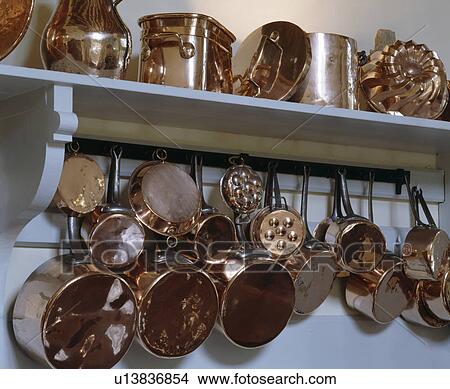 Picture - Close-up of of antique copper pans on hooks below shelf. Fotosearch
