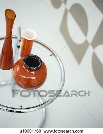 Stock Photo - Close-up of orange glass vases on modern glass and chrome table. Fotosearch