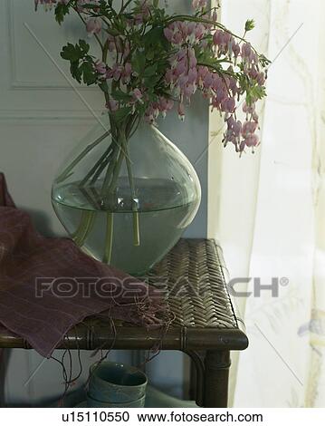 Stock Image - Close-up of pink dicentra in glass vase on wicker table. Fotosearch