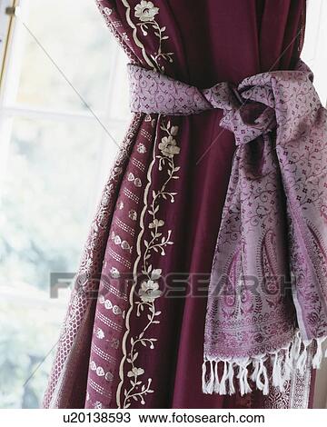 Stock Image - Close-up of red silk curtain with embroidered edging and pink silk tie-back. Fotosearch