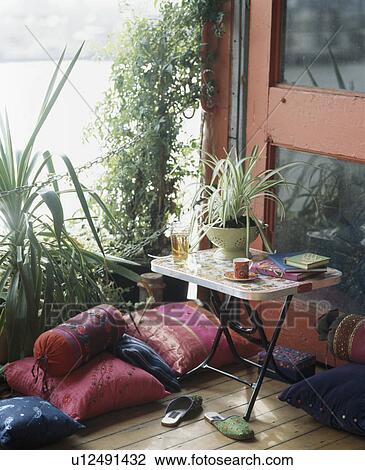 Stock Image - Close-up of small table and pink Indian silk cushions on townhouse balcony. Fotosearch