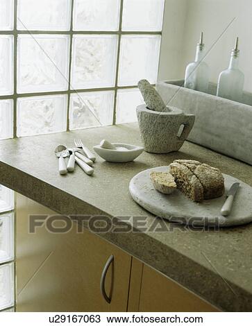 Stock Image - Close-up of stone pestle+mortar and marble breadboard on stone worktop. Fotosearch