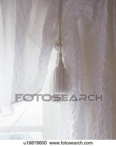 Stock Image - Close-up of white cotton curtains and white tassel. Fotosearch