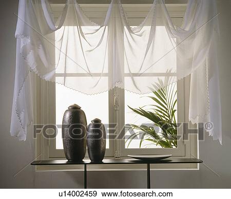 Stock Photo - Close-up of white voile drapes on window above table with black vases. Fotosearch