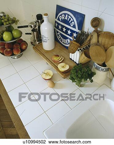Stock Image - Close-up of wooden utensils and fruit on tiered dish on white tiled worktop. Fotosearch