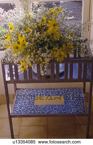 Stock Photography - Close-up of yellow flowers in vase on blue mosaic-tiled table. Fotosearch