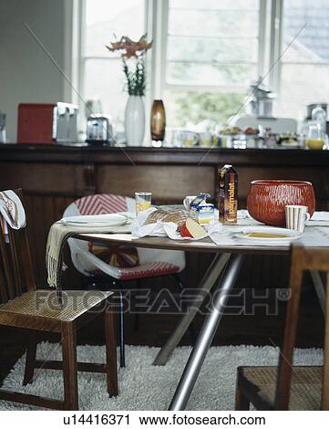 Stock Image - Cluttered table in modern kitchen with brown fitted units. Fotosearch