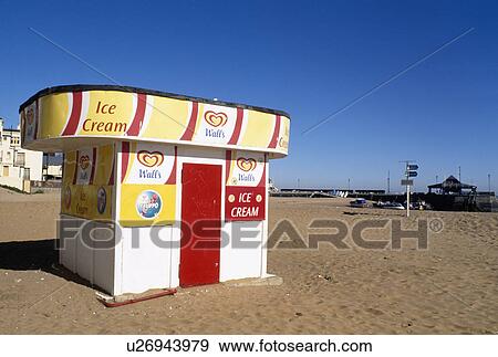 Stock Photo - Colourful yellow and red icecream hut on sandy beach below blue sky at Broadstairs in Kent. Fotosearch