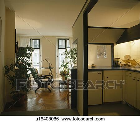 Stock Photograph - Compact fitted kitchen built into corner of large apartment living room. Fotosearch