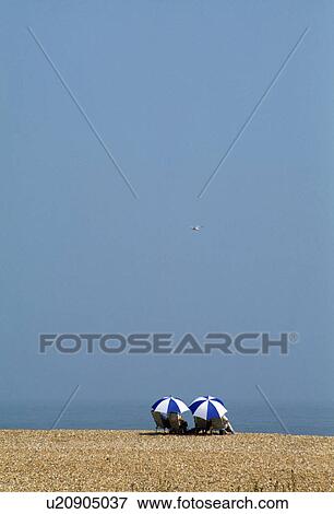 Couple sitting beneath blue & white umbrellas on the beach blue sky at Deal in Kent View Large Photo Image Stock Photo - Couple sitting beneath blue & white umbrellas on the beach blue sky at Deal in Kent. Fotosearch